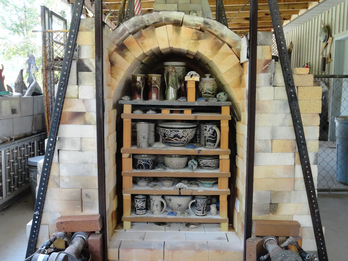 The brick kiln at the studio, arched door open, shelves loaded with pots