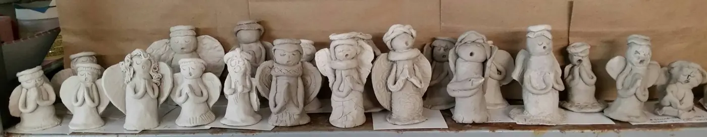 A row of unglazed clay angel figures waiting to be glazed