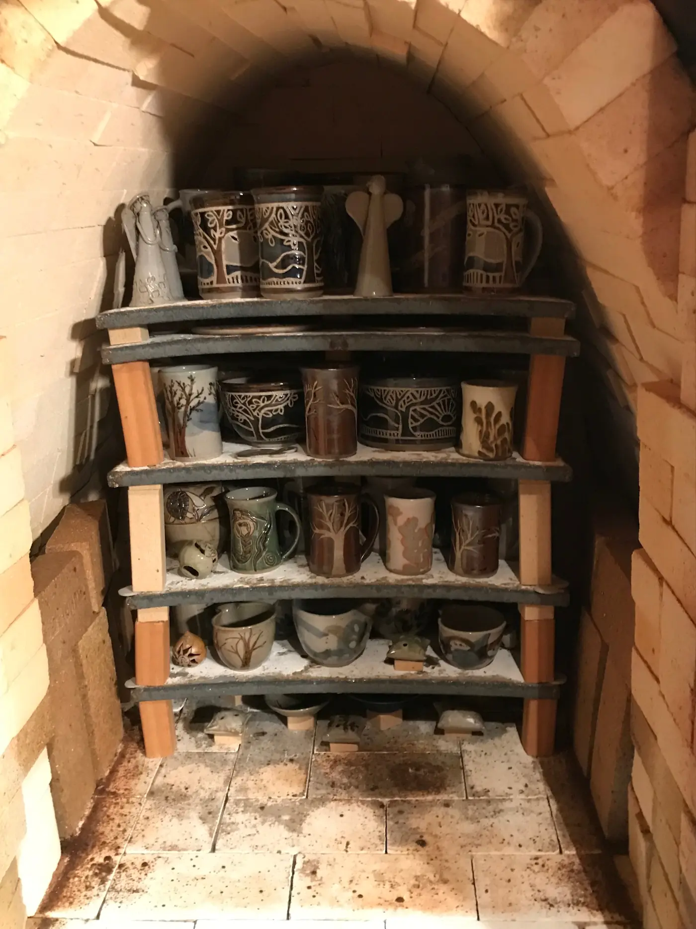 Kiln shelves stacked with glazed mugs and jars before a firing