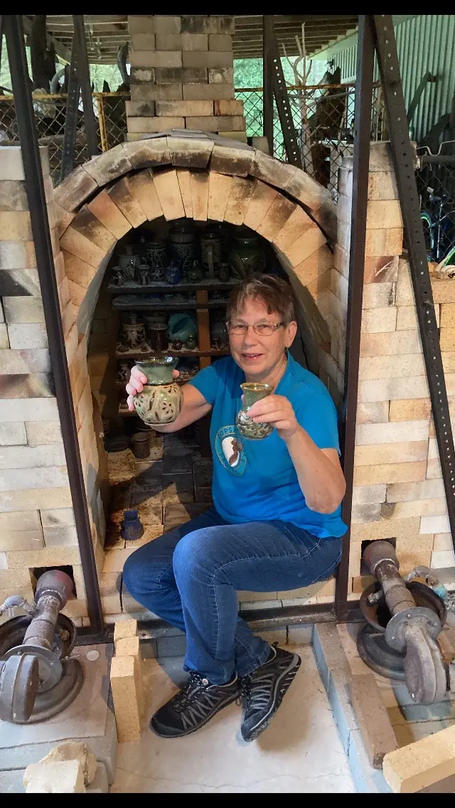 Kathy Whitley sitting inside the brick kiln, holding a mug